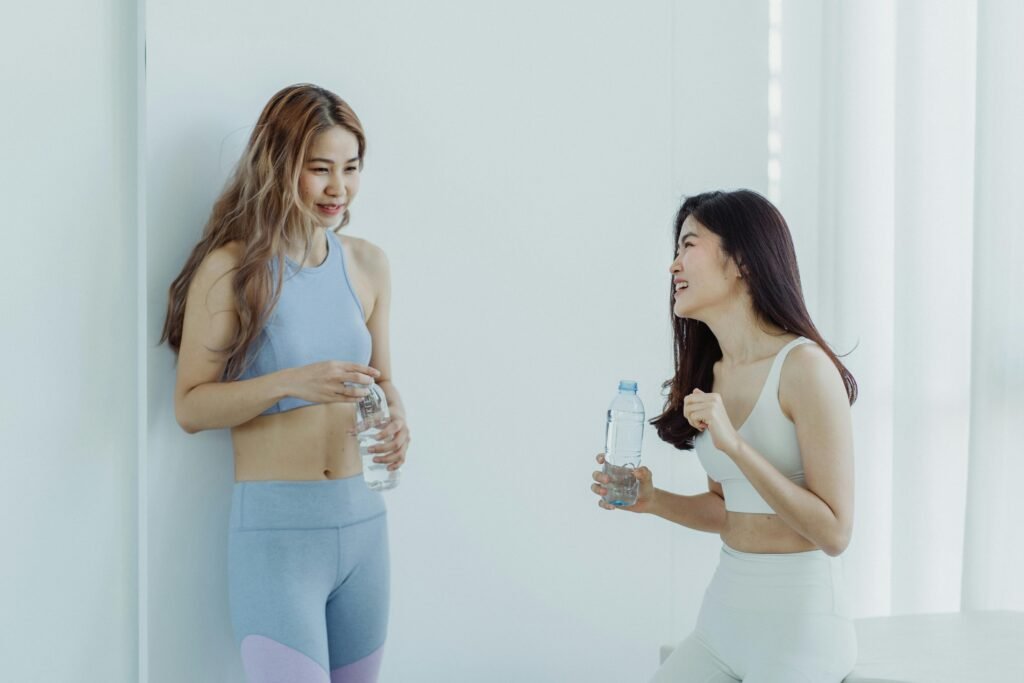 Two Asian women in sportswear chatting with water bottles during a fitness break.