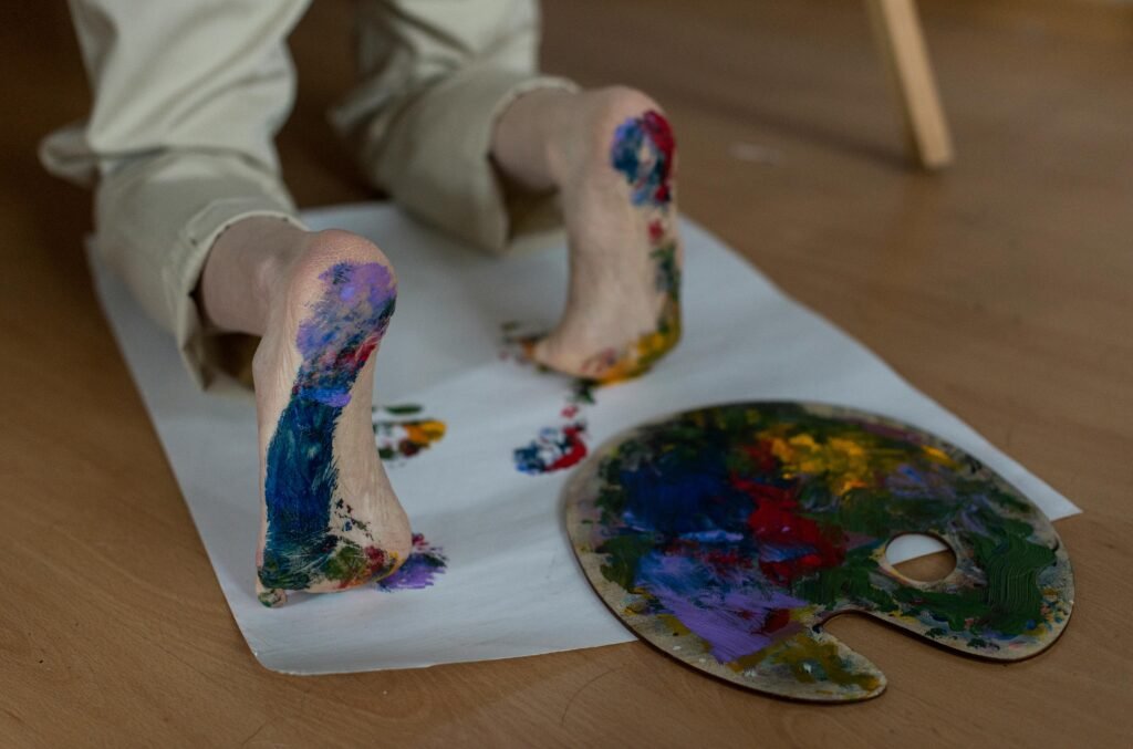 A close-up of feet painting colorful artwork using a palette on paper.